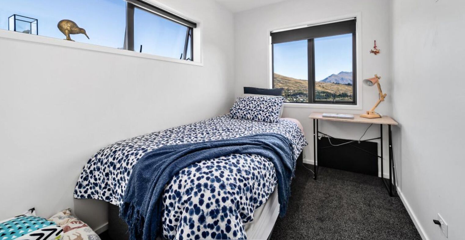 Ein kleines, ordentliches Schlafzimmer mit einem Bett, einem Schreibtisch und einem Fenster mit Bergblick.