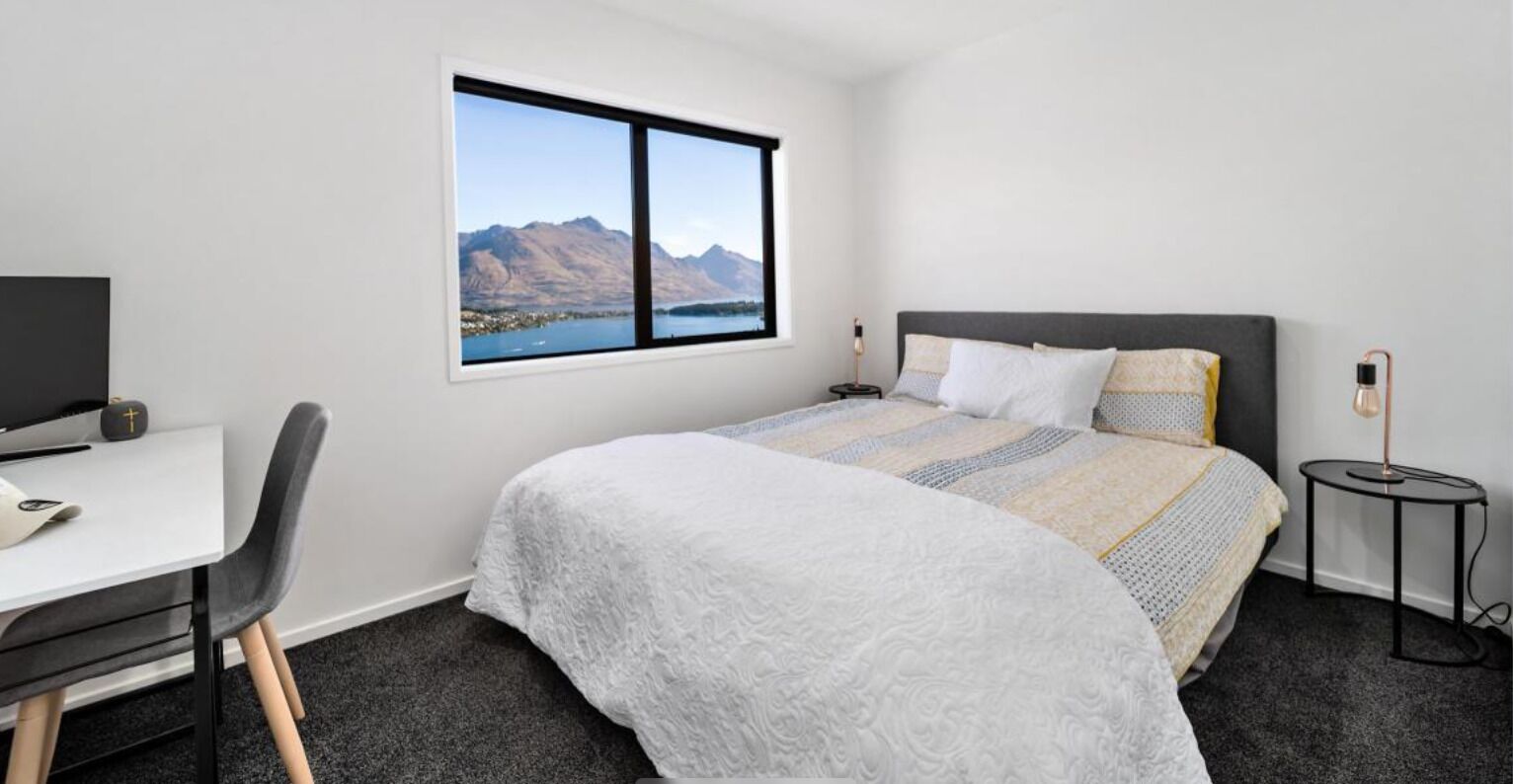 Ein Schlafzimmer mit Bett, Schreibtisch, Stuhl, Lampe und Fenster mit Bergblick.