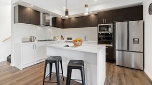 A modern kitchen with white cabinetry, stainless steel appliances, and a central island with stools.