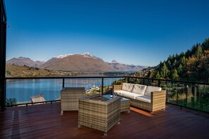 A balcony with wicker furniture, a glass table, and a view of mountains and a lake. - A LUCKIE CHARM - 5-BEDROOM TOWNHOUSE (Queenstown Hill)