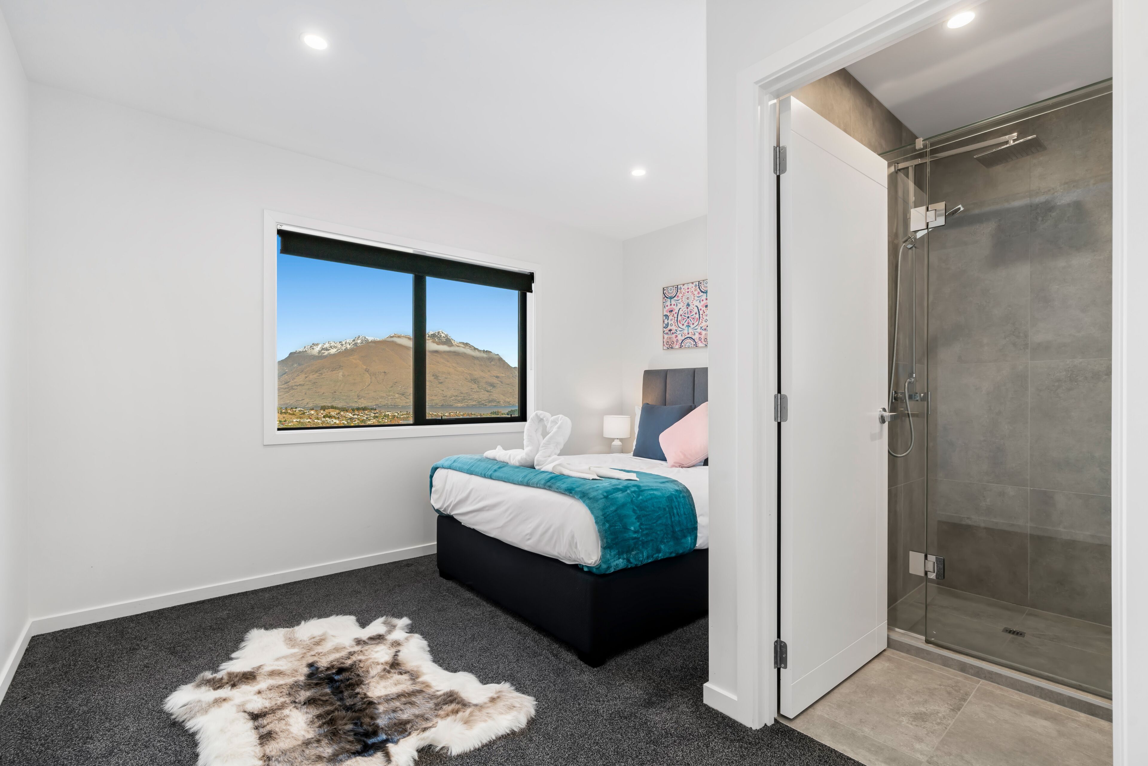 A bedroom with a bed, a window with a mountain view, a glass shower, and a rug.