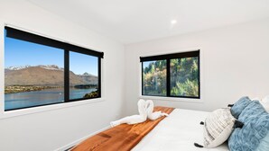 A bedroom with a large bed, two windows with mountain and forest views, and a wooden headboard.