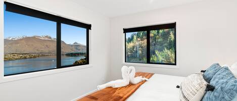 A bedroom with a large bed, two windows with mountain and forest views, and a wooden headboard.