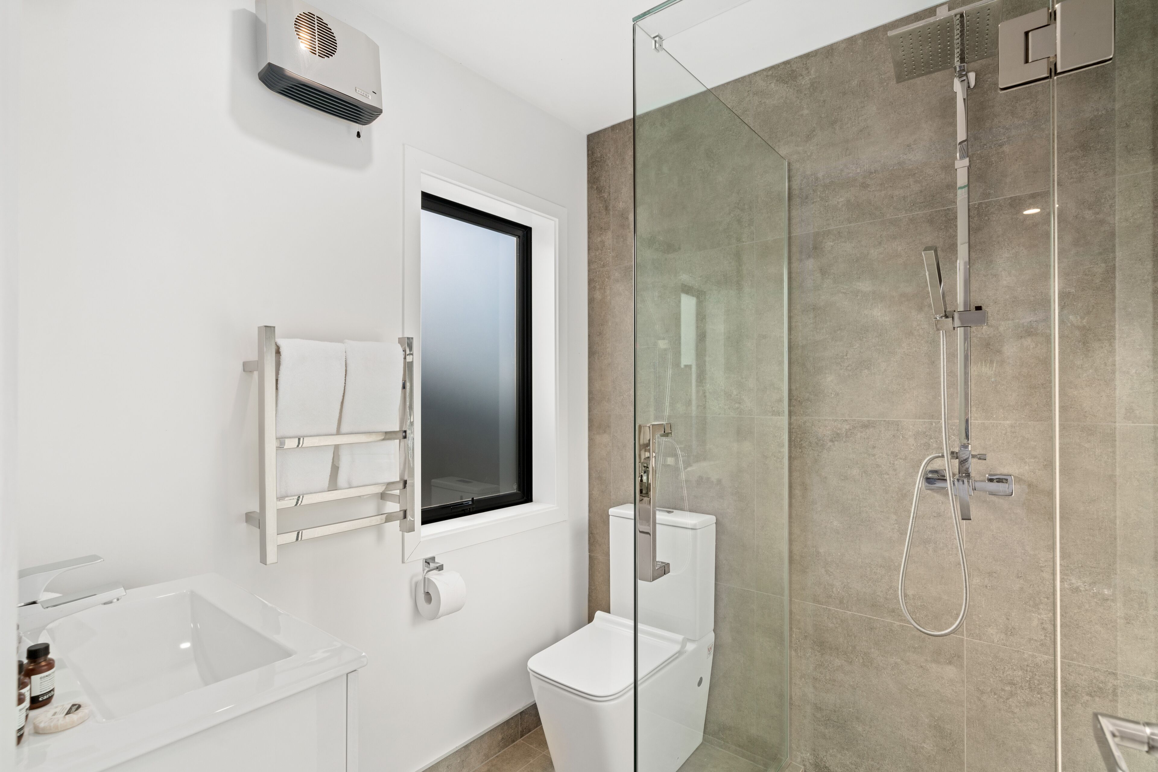A modern bathroom with a glass-enclosed shower, a white sink, and a toilet.