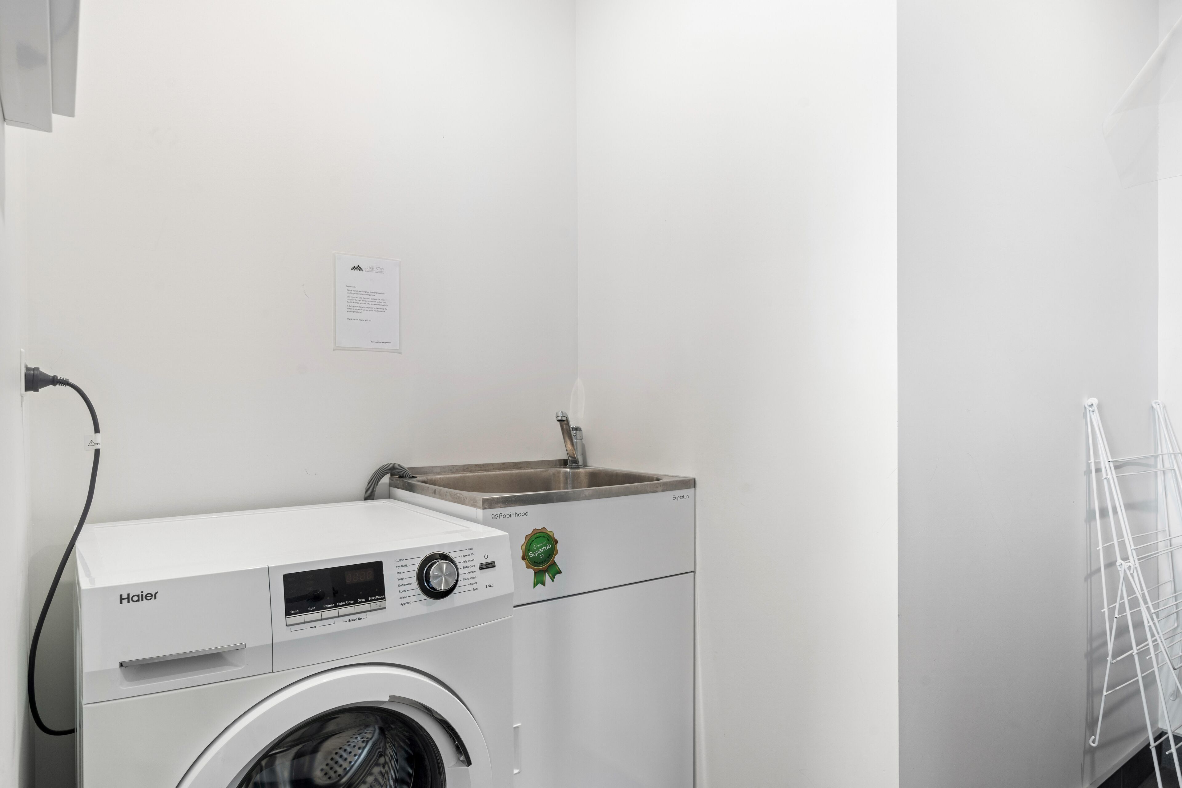 Een kleine wasruimte met een voorlader wasmachine en droger, een wasbak en een droogrek.