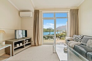 A modern living room with a television, a sofa, a coffee table, and a view of a mountainous landscape through a large sliding glass door.