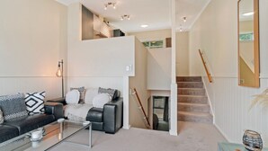 A modern living room with a black leather sofa, a glass coffee table, and a staircase leading to an upper level. - 2-BEDROOM APARTMENT - BEECHWOOD (Queenstown)