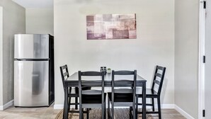 Una cocina compacta con un refrigerador de acero inoxidable integrado, una mesa de comedor con cuatro sillas y un tapete texturizado en el suelo.
