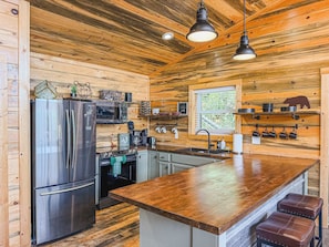 A compact kitchen with a central island, stainless steel appliances, and wooden paneling. - Fall specials/Stunning Views/Luxury/Pet Friendly (Sevierville)