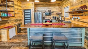 Ein Holzblockhaus-Interieur mit einer zentralen Kochinsel, Barhocker, einem Kühlschrank und einem Fernseher.