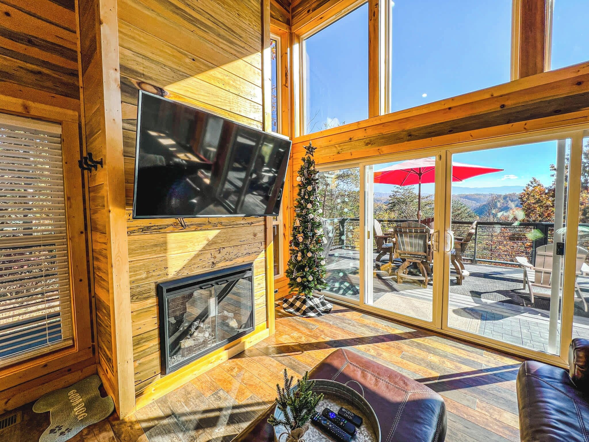 Un interior de madera con chimenea, un televisor y vistas al exterior a través de amplios ventanales.