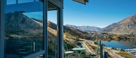 A balcony with a glass door overlooking a mountainous landscape and a lake.