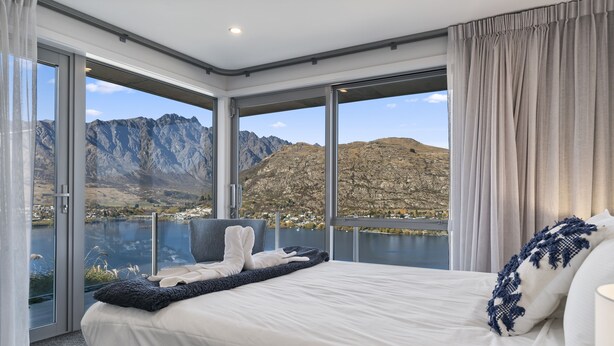 A bedroom with a large bed, a view of mountains and a lake, and a sliding glass door. - MODERN ALPINE LIVING SPECTACULAR VIEW (Queenstown)