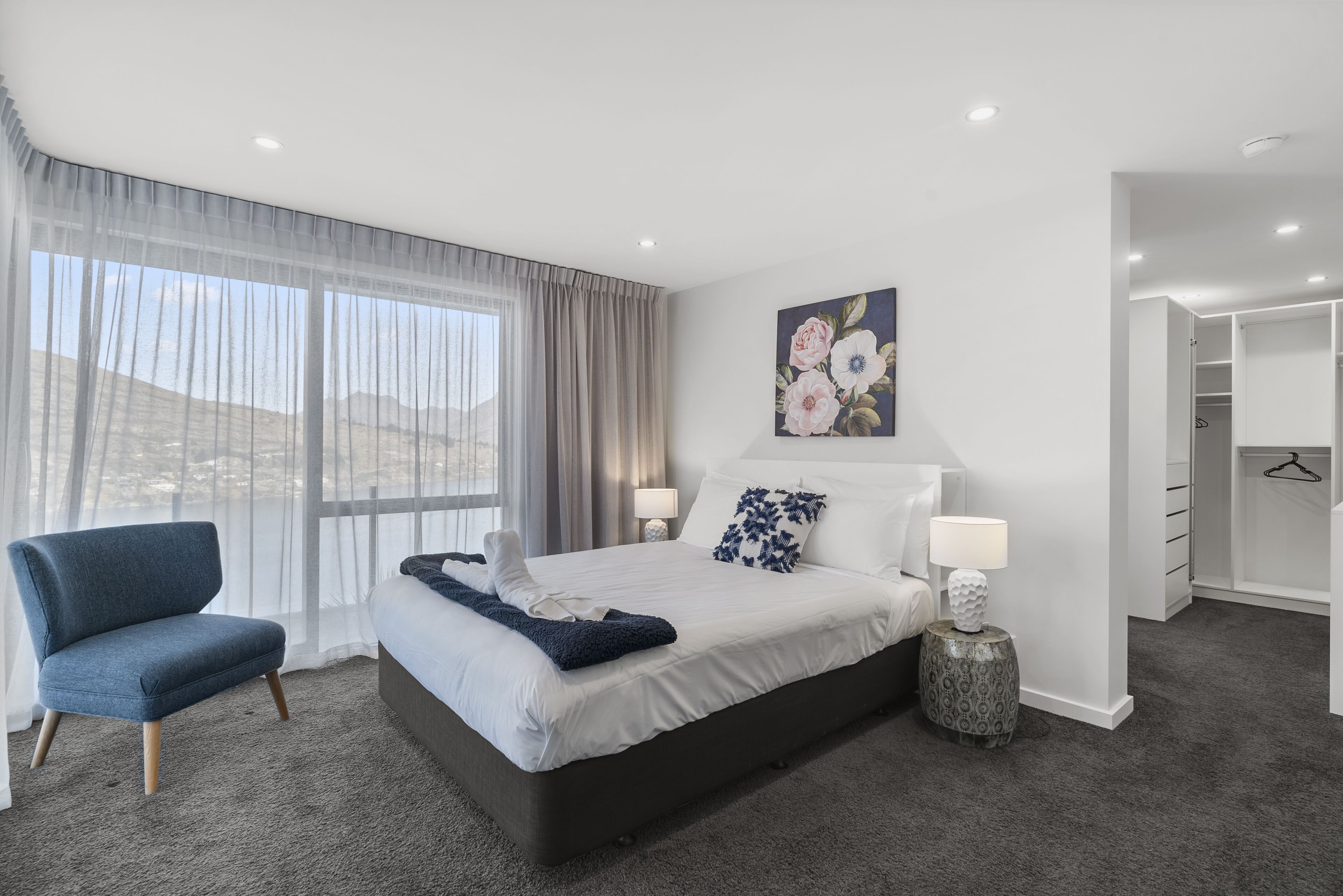 A modern hotel room with a large bed, a chair, a bedside table, and a painting on the wall.