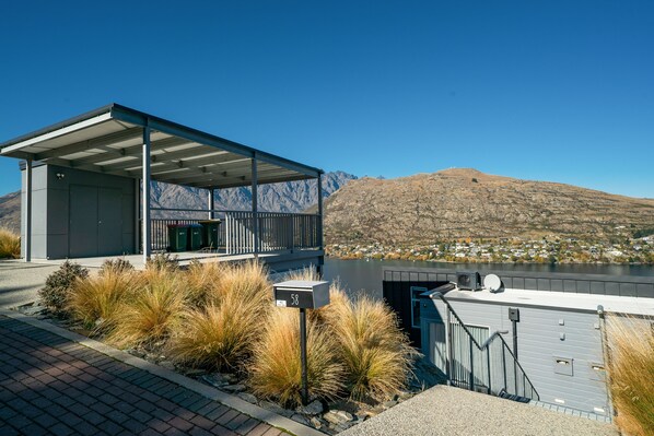 A modern building with a covered outdoor area, a view of a lake, and mountains in the background.
