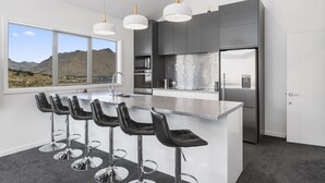 A modern kitchen with a large island, bar stools, stainless steel appliances, and a view of mountains. - MODERN ALPINE LIVING SPECTACULAR VIEW (Queenstown)