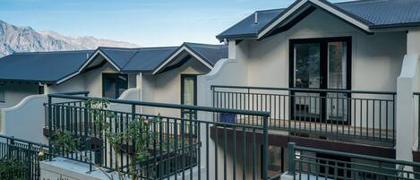A row of modern houses with balconies, a metal railing, and a mountain backdrop.