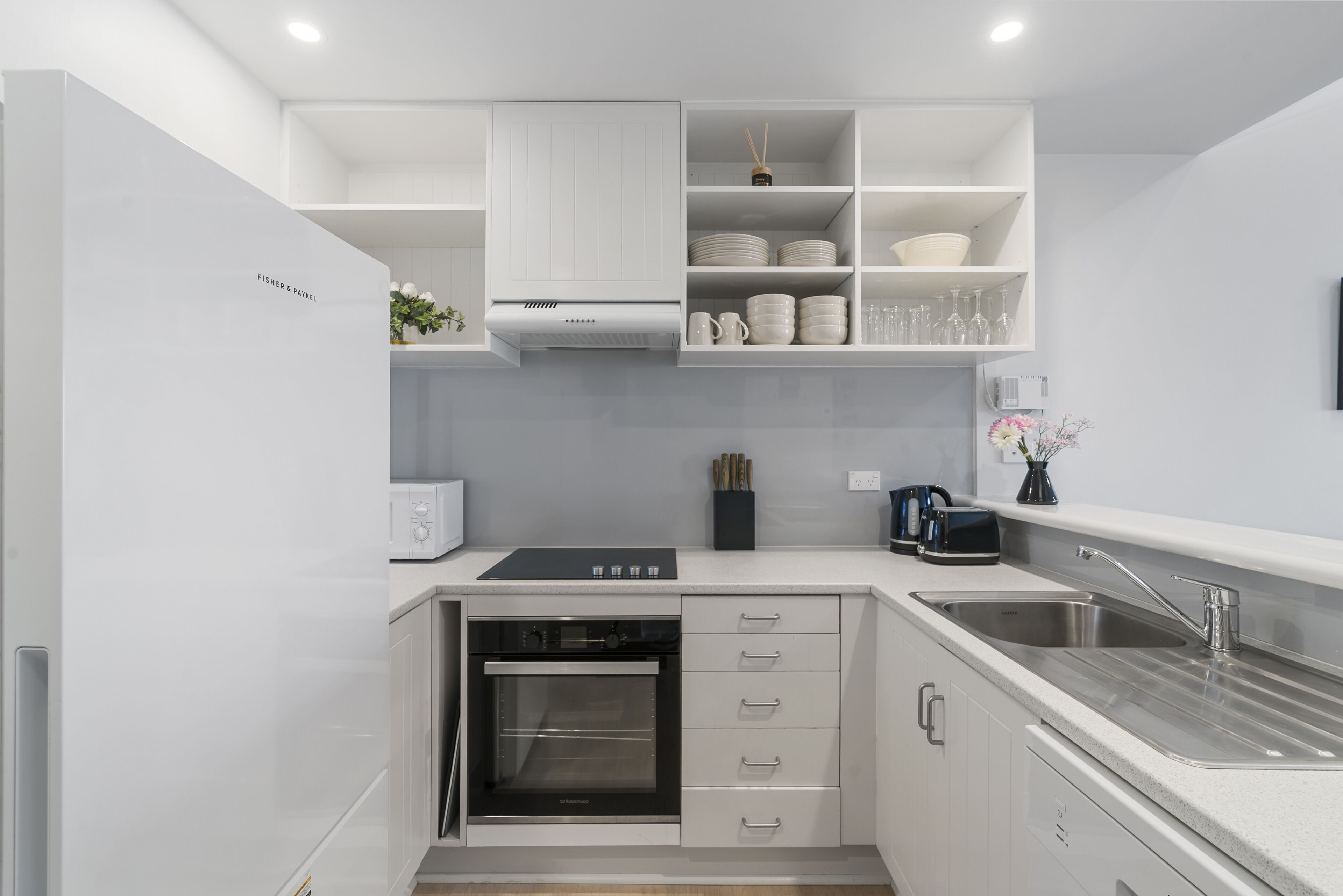 A modern kitchen with white cabinetry, a built-in oven, a sink, and a countertop with a coffee maker.