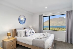 A bedroom with a bed, a nightstand, a wall art piece, and a window with a mountain view.