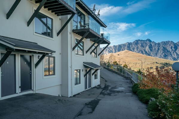 A modern two-story building with large windows and a balcony, set against a mountainous backdrop.