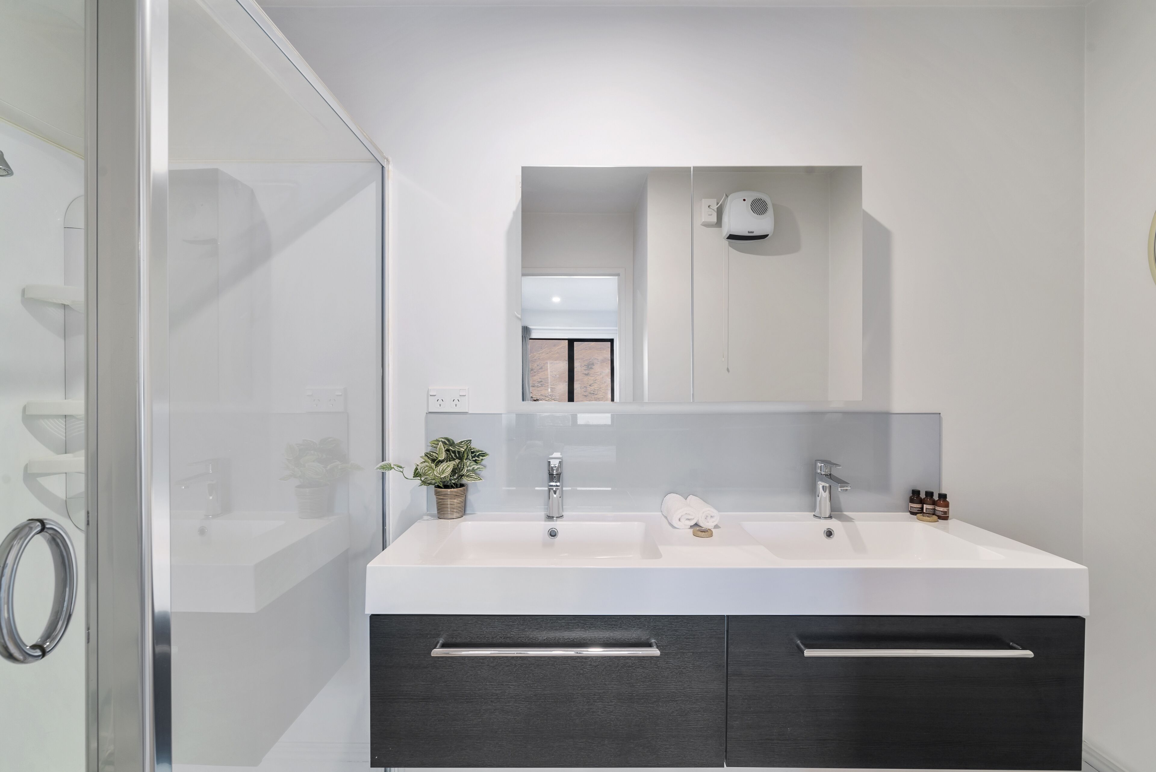 Un baño moderno con cabina de ducha de vidrio, tocador doble y un espejo grande.