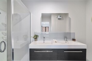 A modern bathroom with a glass shower enclosure, a double sink vanity, and a large mirror.