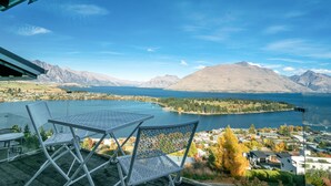 Une terrasse avec deux chaises en métal blanc et une table, donnant sur un lac avec des montagnes en arrière-plan.