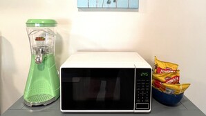 Eine Mikrowelle, ein Mixer und eine Schüssel Chips auf einem Tisch mit einem Palmen-Gemälde an der Wand.