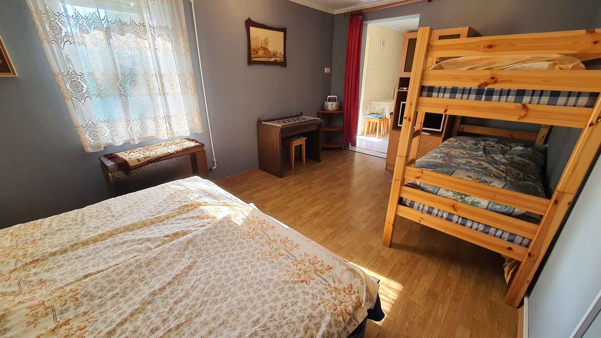 A room with a bunk bed, a desk, a chair, and a window with lace curtains.