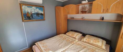 A bedroom with a bed, a wardrobe, a shelf with decorative items, and a painting on the wall.