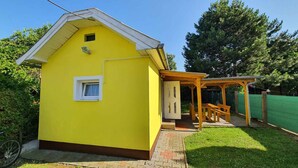 Un bâtiment jaune avec un petit porche et un espace salon abrité.