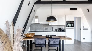 A modern kitchen with white cabinets, a wooden dining table, two black chairs, and a hanging pendant light.