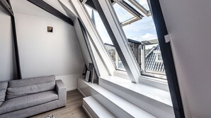 A modern loft bedroom with skylights, a gray sofa, and a view of the city skyline.