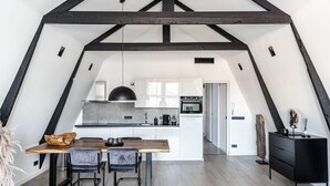 A modern kitchen with white cabinets, a black oven, and a wooden dining table with two chairs.