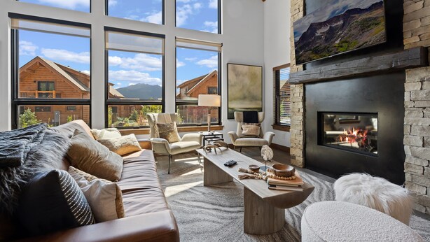 Ein geräumiges Wohnzimmer mit Kamin, großen Fenstern und Bergblick.