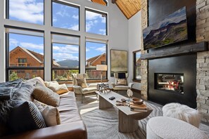 Un salon spacieux doté d’une cheminée, de grandes fenêtres et offrant une vue sur les montagnes.