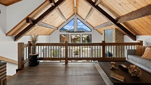 Ein geräumiges Loft mit hoher Decke, Holzbalken, einem Balkon mit Aussicht und einer gemütlichen Sitzecke.