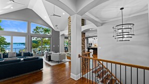 A spacious living area with a large window overlooking a scenic view, a modern staircase, and a kitchen area. - Sunset on Ballycastle w/Heated Pool & Optional Boat Rental (Mooresville)