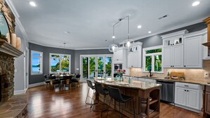 A spacious kitchen with a large island, white cabinets, and a stone fireplace. - Sunset on Ballycastle w/Heated Pool & Optional Boat Rental (Mooresville)