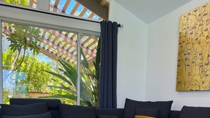 A modern living room with a dark-colored sofa, a glass coffee table, and a large window with a view of greenery outside. - Cheerful four bedroom house with charming view! (Santa Clarita)