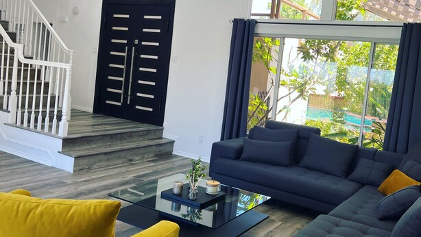 A modern living room with a dark sofa, yellow armchair, and a glass coffee table. A staircase with white railings leads to an upper floor. - Cheerful four bedroom house with charming view! (Santa Clarita)