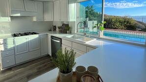 A modern kitchen with white cabinets, a large island, and a view of a swimming pool. - Cheerful four bedroom house with charming view! (Santa Clarita)
