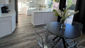 A modern kitchen with white cabinetry, a central island, and a dining area with a round table and chairs. - Cheerful four bedroom house with charming view! (Santa Clarita)