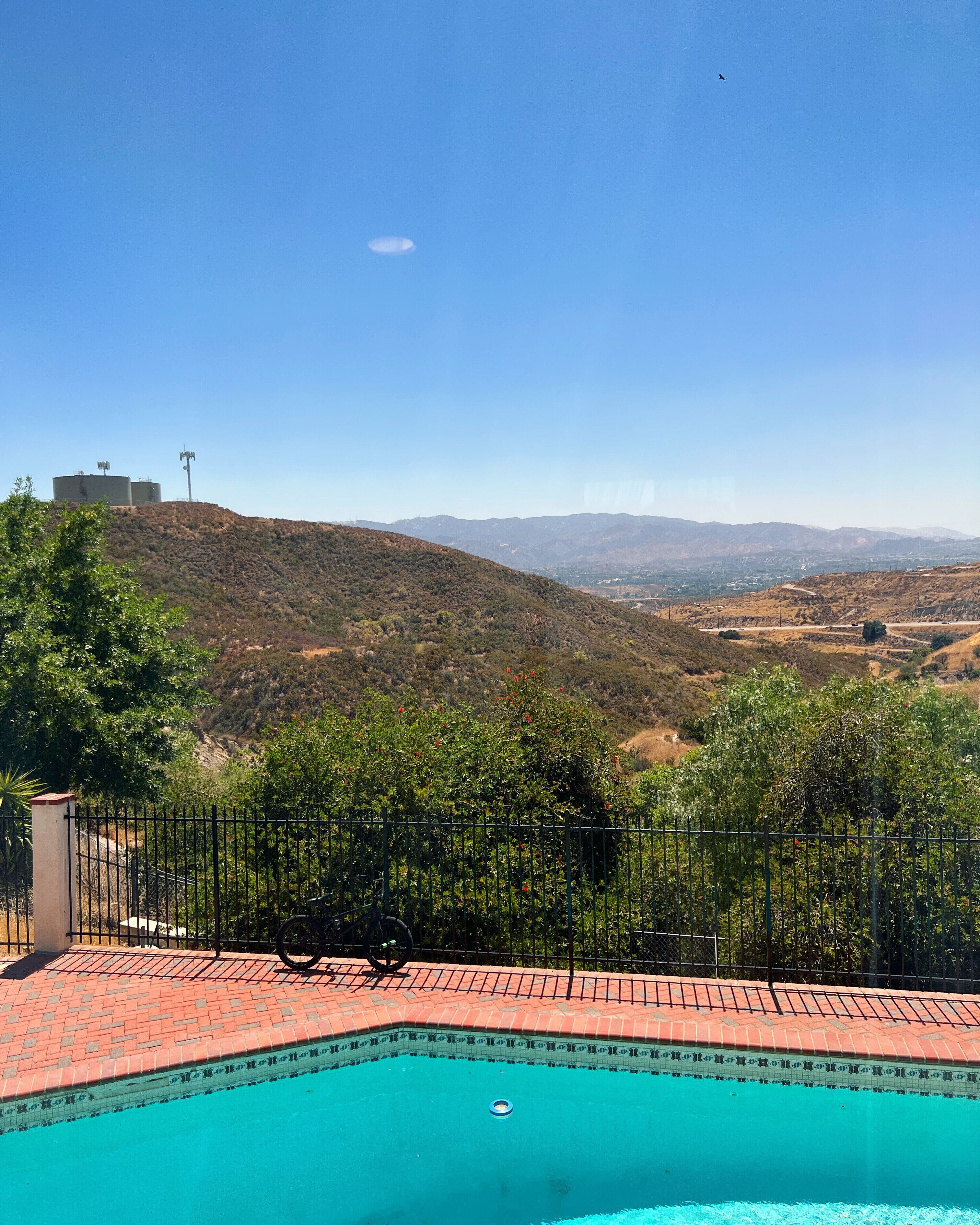 Una piscina con vista su un paesaggio collinare, una recinzione e della vegetazione.