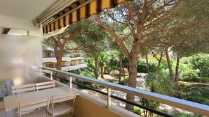 Un balcón con mesa y sillas, con vistas a un jardín con árboles y un edificio al fondo.