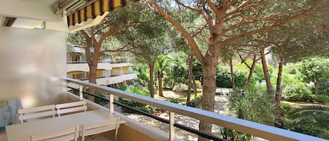 A balcony with a table and chairs, overlooking a garden with trees and a building in the background.