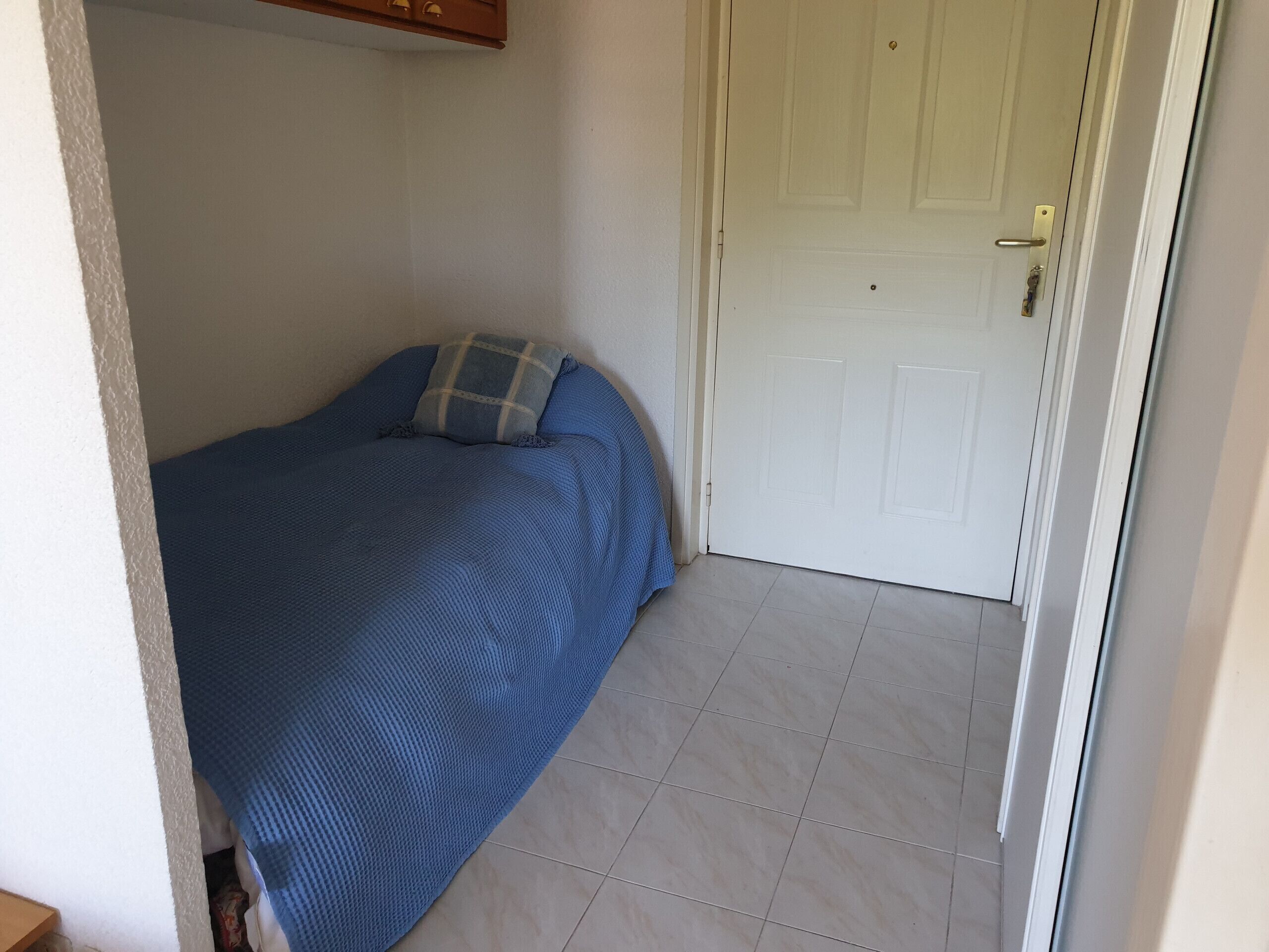 Ein kleines, ordentlich eingerichtetes Schlafzimmer mit Bett, einer Tür und Fliesenboden.