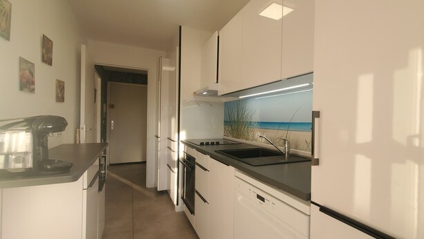 Een moderne keuken met witte kastjes, een zwart aanrecht en uitzicht op zee door een raam.