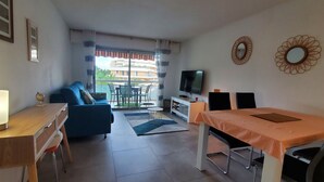 Een woonkamer met een bank, televisie, eettafel en een balkon met uitzicht op gebouwen.
