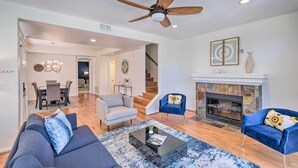 Un salon moderne avec une cheminée, un ventilateur de plafond et un coin repas à l’arrière-plan.